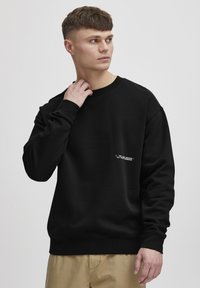 Mustarmüts puuvilla segust, ümar kaelus, pikad varrukad, ribaga mansetid ja alläär, rinnal valge tekstiga detail.
