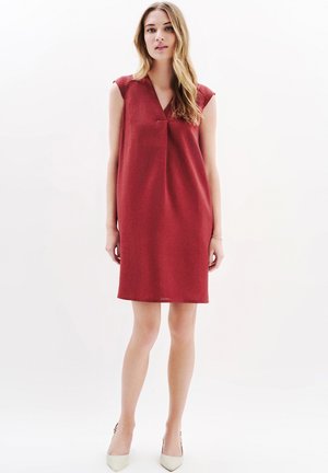Rotes ärmelloses Kleid mit V-Ausschnitt, lockerer Passform und strukturiertem Stoff. Besitzt subtile Faltenlegung an der Brust und endet oberhalb des Knies.