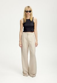 Čierny rebrovaný crop top v kombinácii s béžovými širokými nohavicami s vysokým pásom. Modelka má tiež na sebe čierne slnečné okuliare. Jednoduchý, moderný siluet.