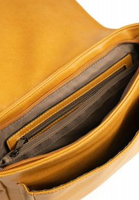Intérieur d'un sac en cuir jaune avec plusieurs compartiments, y compris une poche zippée et un doublure lisse. Présente des coutures contrastées et un design épuré.