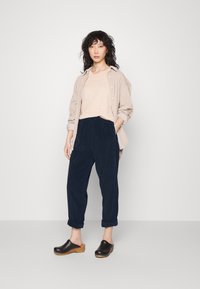 Beige nööpidega särk heleda beeži topi peal, tumesinised korduroo püksid ja mustad puidust klompide kergelt puidust tallaga. Lihtne disain ja tekstuurid.