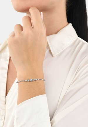 Pulsera de plata con cinco acentos de piedras transparentes, diseño elegante con eslabones retorcidos, llevada en una muñeca, sobre un fondo claro.