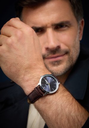 Silver watch with a dark blue dial, silver hour markers, and a brown leather croc-embossed strap. The watch face displays date functionality.