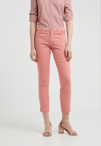 Pantalones encajados de color rosa con una textura suave, de longitud ligeramente recortada, combinados con sandalias de tacón cuadrado beige. Camisa a rayas por encima.