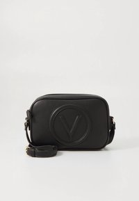 Svart läderaxelväska med texturerad yta, rektangulär form, präglad cirkulär logotyp, justerbar rem och detaljer i guldmetall.