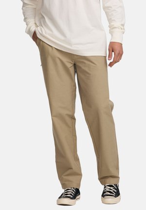 Beige katoenen broeken met een rechte pasvorm, voorzien van zijzakken en een ritssluiting, gecombineerd met zwarte sneakers met een lage schacht.