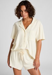 Korte mouwen, knopenpajamaset in een zachte beige stof. Bevat een borstzak en shorts met elastische tailleband voor comfort en gemak.