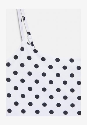 Bílá látka s černými puntíky a nastavitelnými tenkými ramínky, součástí bezrukávového oděvu.