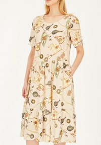 Beżowa sukienka z krótkimi rękawami, z powtarzającym się wzorem kolorowych obiektów. Projekt obejmuje kieszenie i zwiewną spódnicę.