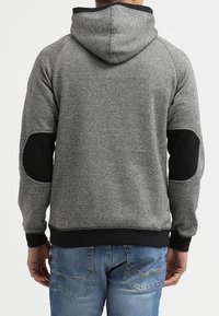 Sudadera gris y negra con un patrón texturizado, mangas raglán y parches en los codos. Presenta una capucha con cordón y un dobladillo acanalado.