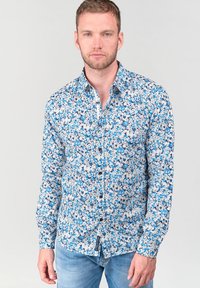 Camicia button-up blu a fiori con intricati motivi floreali bianchi e blu scuro, maniche lunghe e colletto a punta; tessuto leggero.