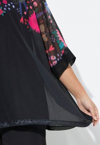 Copertura nera trasparente con motivi floreali e geometrici colorati sulle maniche, caratterizzata da una texture liscia e un design leggero e svasato.