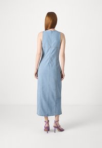 Lys blå denim maxi-kjole med en tettsittende silhuett, uten ermer, og synlige sømdetaljer. Kombinert med lilla sandaler med høye hæler og stropper.