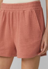 Terrakotta-Shorts mit einer strukturierten Oberfläche, elastischem Bund und Seitentaschen. Hervorzuheben ist der leichte Stoff und der lockere Schnitt.