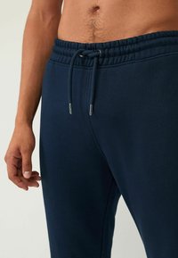Joggers de algodón azul marino con cintura elástica y cordón; textura suave y diseño ajustado. Mano visible descansando sobre la tela.