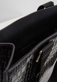 Sac à main noir à texture de crocodile avec un intérieur lisse, doté d'une poche zippée et de plusieurs compartiments pour l'organisation.