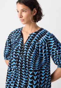 Abito blu e nero con motivo, scollo a V, maniche corte a sbuffo e design arricciato. Realizzato in un tessuto leggero e strutturato.