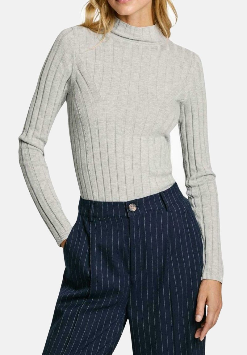 Siv krožen dolg rokav z visokim ovratnikom, v kombinaciji s temno modrimi hlačami z ožjimi črtami in gumbom.