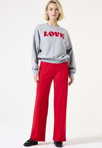 Sweat-shirt gris avec le mot "LOVE" en lettres rouges, associé à un pantalon rouge taille haute avec des coutures latérales. Le mannequin se tient avec une expression neutre.