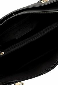 Intérieur d'un sac à main noir montrant des compartiments zippés et une fermeture à glissière dorée, avec une étiquette de marque cousue à l'intérieur.