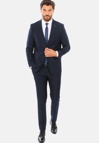 Abito blu navy con design slim fit, giacca monopetto, cravatta abbinata e scarpe nere lucide, con una finitura in tessuto liscia.