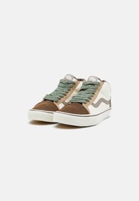 Zapatillas altas con punteras de ante marrón, paneles crema, acentos beige y cordones verdes sobre un fondo blanco.