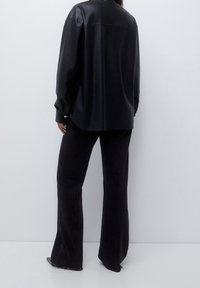 Chemise en cuir noir à coupe décontractée, dotée d'un col plat et de poignets boutonnés, associée à un pantalon en denim noir à jambes larges.