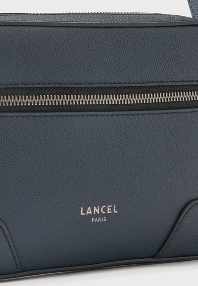 Крупен план на тъмносивата кожена чанта Lancel Paris, показващ текстурираната ѝ повърхност и хоризонталния сребрист цип.