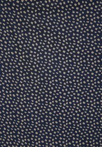 Marineblauwe stof met een verspreid patroon van kleine beige stippen, wat een gestructureerde uitstraling geeft. Zachte, lichte textiel met een gladde afwerking.