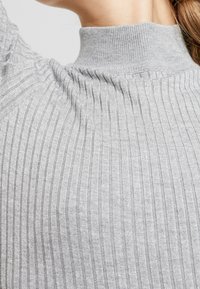Pull gris côtelé avec un col montant et un tissu texturé. Le motif se compose de rayures verticales pour plus de détails.