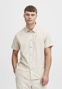 Korte mouwen beige knoopshirt gemaakt van gladde stof, met een kraag, voorknopjes en een subtiel zijlabel.