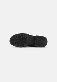 Black rubber shoe sole featuring a textured, patterned design with raised grips for traction. Smooth upper section with a flexible middle.