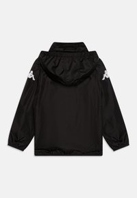 Veste coupe-vent noire avec capuche, poignets élastiques et ourlet élastique, présentant des accents de logo blancs sur les épaules. Matière lisse et légère.