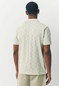 Kortærmet skjorte i lys beige stof med et gentaget solmønster. Skjorten har en afslappet pasform og en klassisk krave.