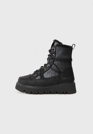 Schwarze knöchelhohe Stiefel mit Kunstfellfutter, Obermaterial aus Wildleder und gemustertem Textil, Metallbeschläge und dicke Gummisohle.