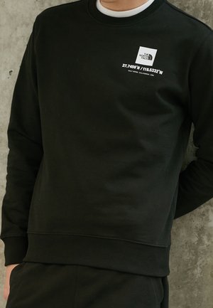 Zwarte sweatshirt gemaakt van zacht materiaal, met geribbelde boorden en zoom. Versierd met een wit logo en geografische coördinaten op de voorkant.