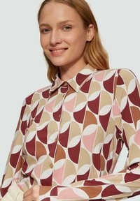 Overhemd van een zachte stof, met een geometrisch patroon in bordeauxrood, roze, beige en witte tinten; klassieke kraag en ronde onderkant.