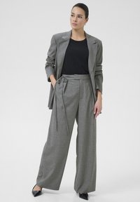 Blazer gris a rayas con pantalones anchos de cintura alta a juego, combinado con una blusa negra y tacones de punta negra.