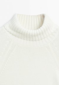 White knitted turtleneck sweater with ribbed collar and detailed stitching on shoulders and sleeves visible.