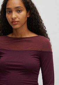 Burgunderfarbener Langarmshirt mit transparenter Halslinie, figurbetontem Schnitt und glatter Textur. Bemerkenswerte Details umfassen ein U-Boot-Ausschnitt-Design.