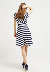 Kjol i marinblått och vitt randigt mönster med V-ringning och utsvängd kjol. Tillverkad av mjukt tyg, har korta ärmar och en figurnära midja.