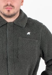 Giacca camicia in pile grigio scuro con superficie testurizzata, chiusura con bottoni, colletto e un piccolo logo sulla tasca del petto.