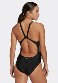 Maillot de bain une pièce noir avec un dos ouvert et bas, des bretelles croisées fines, et une coupe ajustée. Tissu lisse avec un design minimaliste.