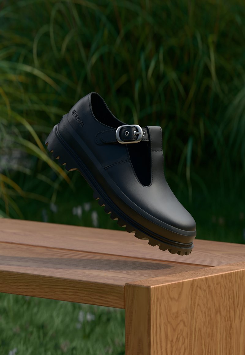 Μαύρο δερμάτινο παπούτσι με πόρπη, στρογγυλή μύτη και ανθεκτική σόλα. Ο σχεδιασμός διαθέτει ιμάντα T και λείο υλικό.