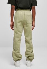 Light green sweatpants made of cotton blend, featuring an elastic waistband and a single back pocket. Worn with white sneakers.
