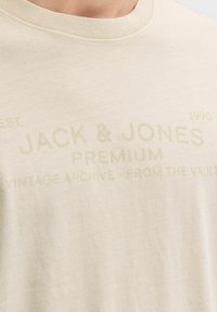 Beiges Baumwoll-T-Shirt mit Rundhalsausschnitt, versehen mit helltonigem Markentext: "JACK & JONES PREMIUM VINTAGE ARCHIVE - FROM THE VAULT."