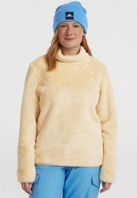 Fleece hoodie in lichtgeel met een hoge hals en lange mouwen. Zachte textuur met een gezellige uitstraling. Draagt met blauwe broek en een bijpassende muts.