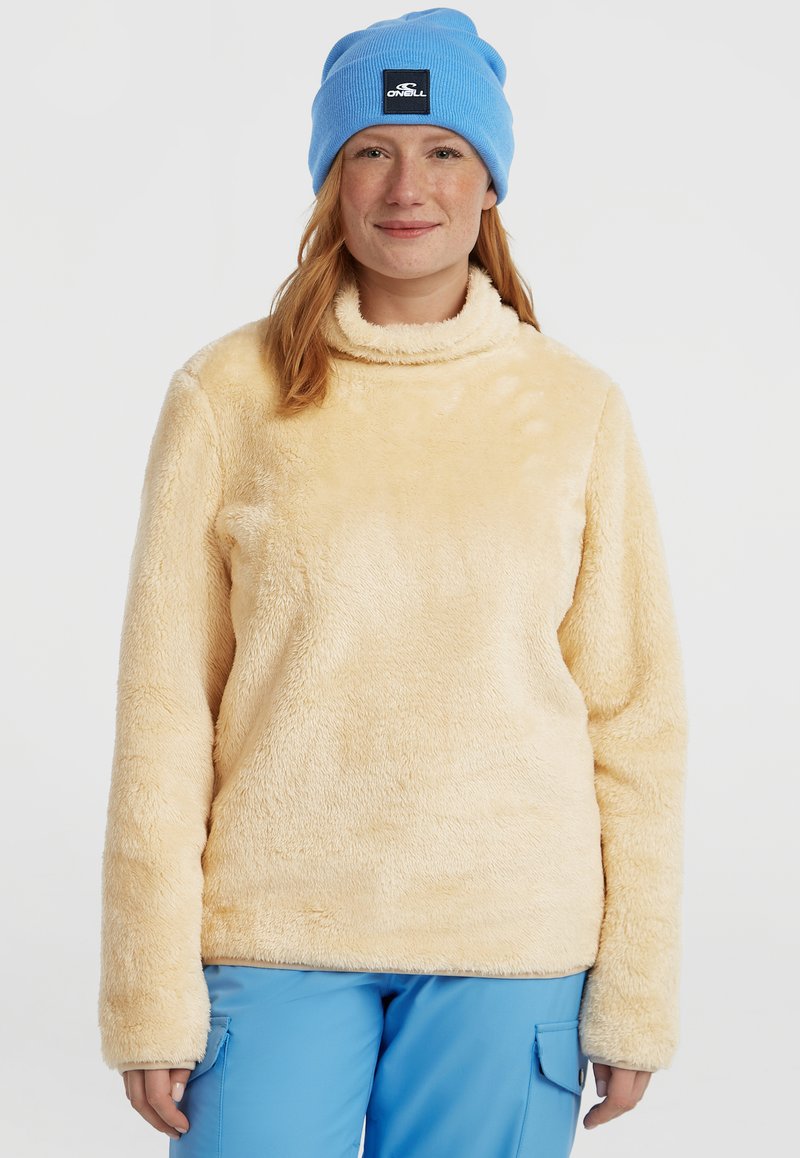 Fleece pullover i lys gul med høj hals og lange ærmer. Blød tekstur med en hyggelig følelse. Båret med blå bukser og en matchende hue.