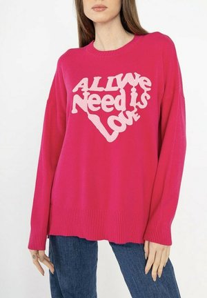 Pull fuchsia avec une coupe décontractée, présentant un grand motif en forme de cœur crème avec l'inscription "TOUT CE DONT NOUS AVONS BESOIN, C'EST L'AMOUR." Ourlets et poignets côtelés.