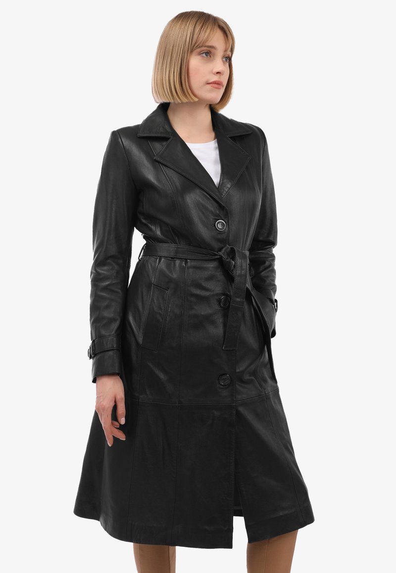 Zwarte leren trenchcoat met een tailleband, grote revers en knopen aan de voorkant. Beschikt over twee zijzakken en een lengte tot halverwege het kalf. Gladde textuur.